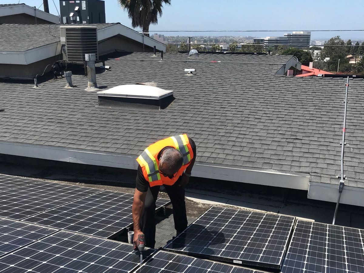 An installer fixing a panel to the mounting rails on a shingle roof